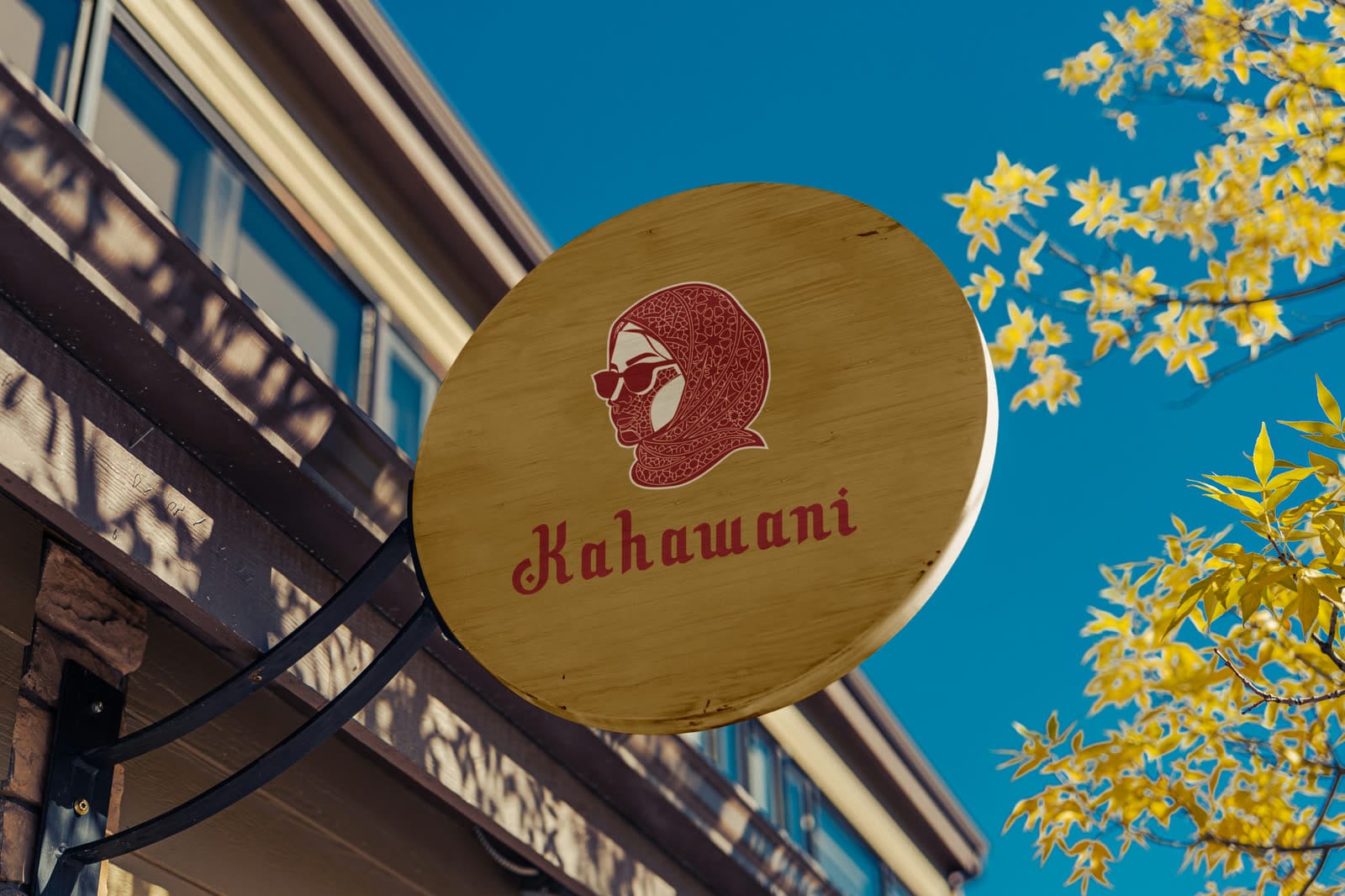 Round wooden hanging sign with a red portrait of a woman in a patterned hijab and sunglasses, and the Kahawani wordmark.